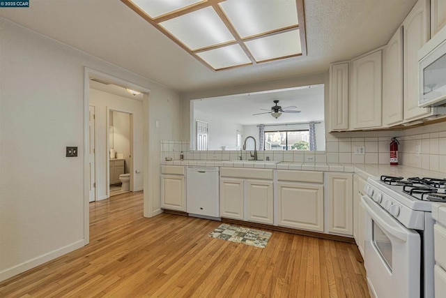 kitchen with white cabinetry, sink, light wood-type flooring, backsplash, and white appliances