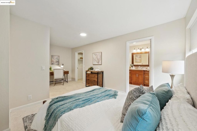 bedroom with sink, a spacious closet, light colored carpet, and ensuite bathroom