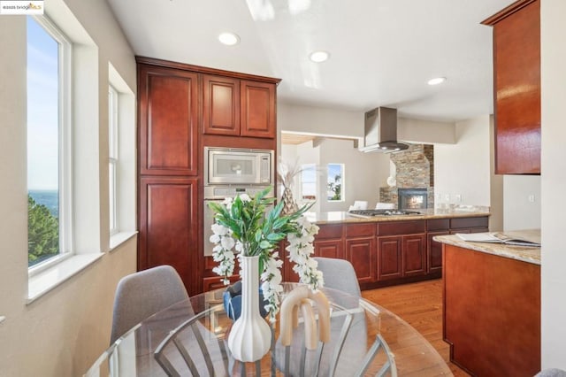 kitchen with light hardwood / wood-style floors, stainless steel appliances, exhaust hood, and light stone countertops