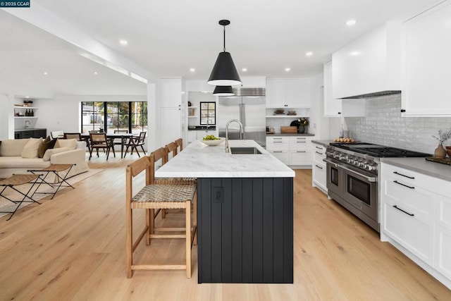 kitchen with premium range hood, a kitchen bar, decorative light fixtures, a center island with sink, and premium appliances