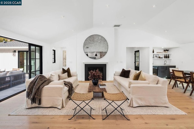 living room featuring vaulted ceiling, sink, and light hardwood / wood-style flooring