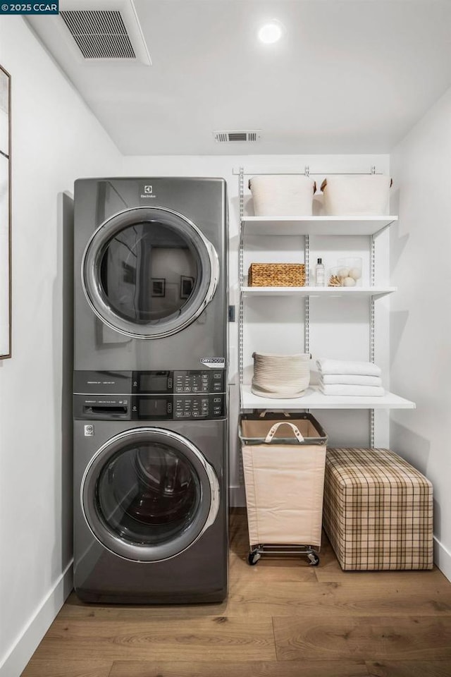 clothes washing area with hardwood / wood-style flooring and stacked washer and clothes dryer