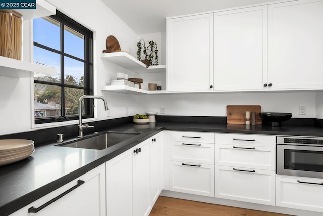 kitchen featuring white cabinetry, sink, stainless steel oven, and light hardwood / wood-style floors