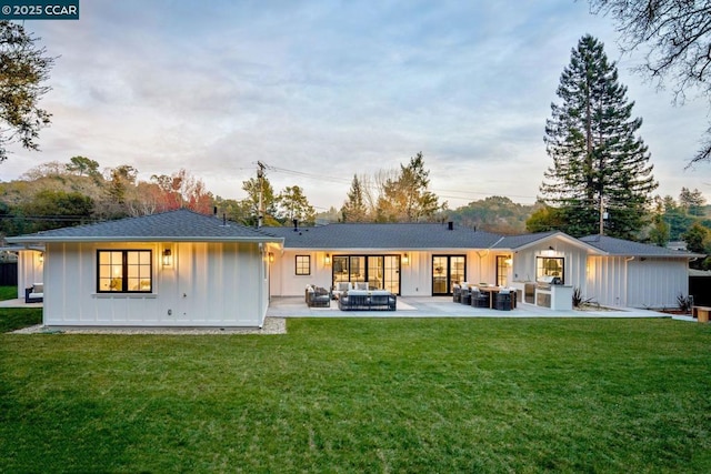 back house at dusk with an outdoor living space, a patio, and a yard