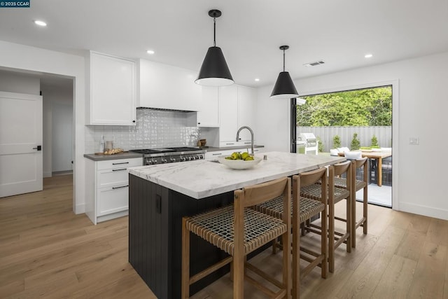 kitchen featuring white cabinetry, light stone counters, decorative light fixtures, a kitchen island with sink, and light hardwood / wood-style floors