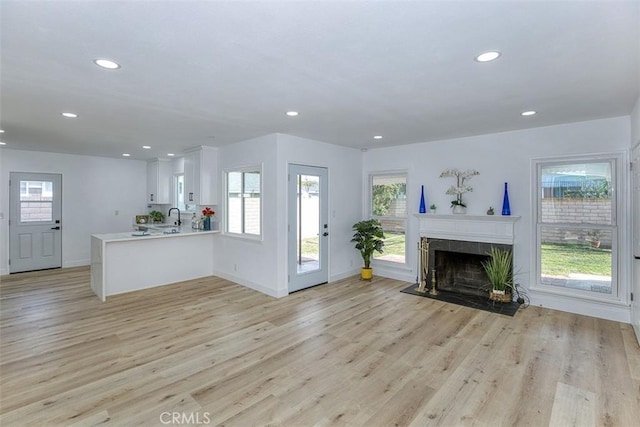 unfurnished living room with a tiled fireplace, sink, and light wood-type flooring