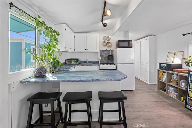 kitchen with black microwave, a peninsula, white cabinetry, freestanding refrigerator, and a kitchen bar