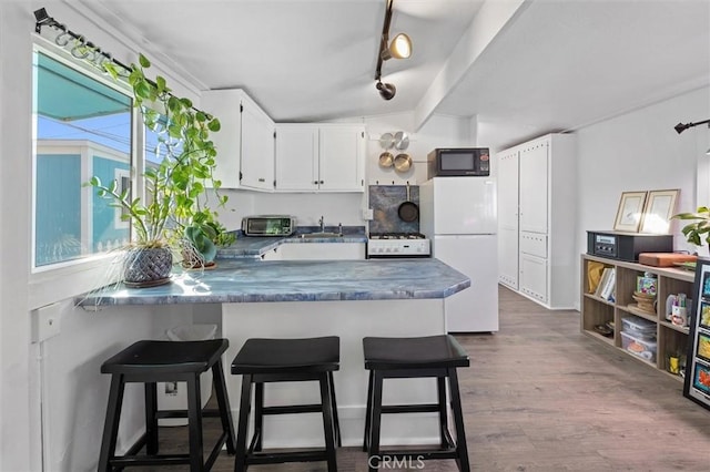 kitchen featuring a sink, dark countertops, white cabinetry, white appliances, and a peninsula