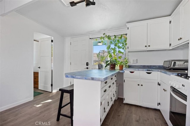 kitchen with a kitchen bar, dark wood-type flooring, white cabinets, and wall oven