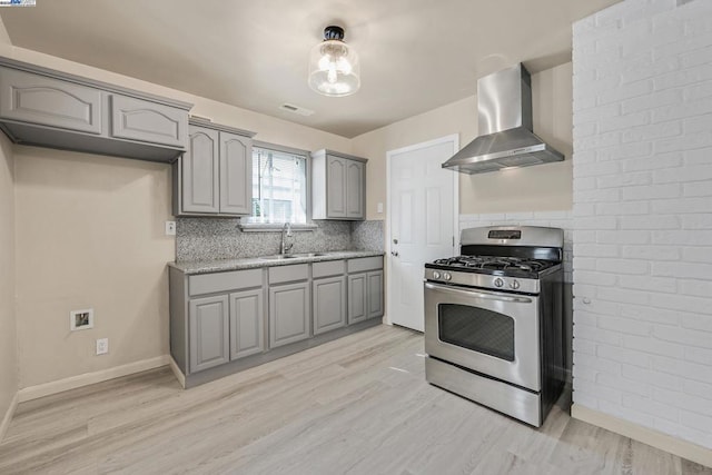 kitchen featuring wall chimney exhaust hood, gray cabinets, sink, and stainless steel gas range oven