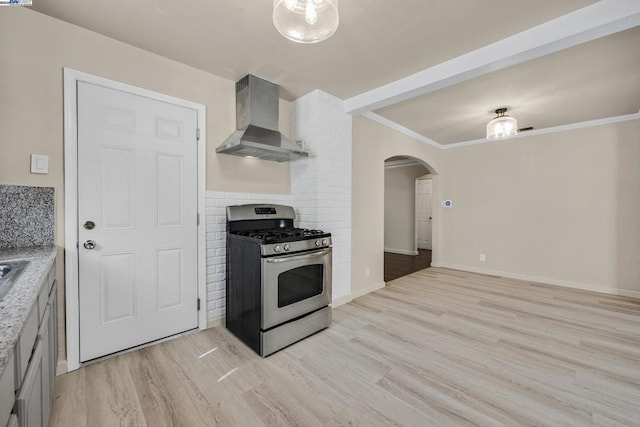 kitchen featuring backsplash, crown molding, stainless steel gas range oven, wall chimney range hood, and light hardwood / wood-style flooring