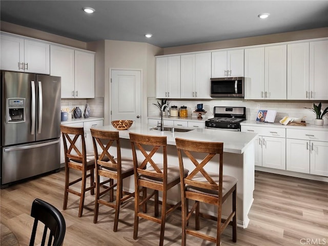 kitchen with stainless steel appliances, white cabinetry, a kitchen island with sink, and backsplash