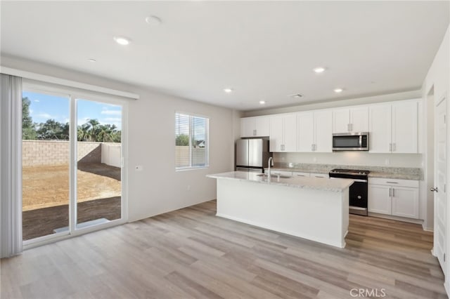 kitchen featuring sink, appliances with stainless steel finishes, an island with sink, light stone countertops, and white cabinets