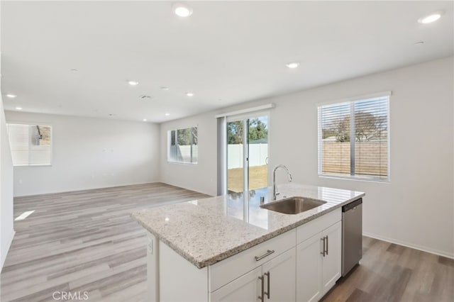 kitchen featuring dishwasher, an island with sink, sink, white cabinets, and light stone countertops