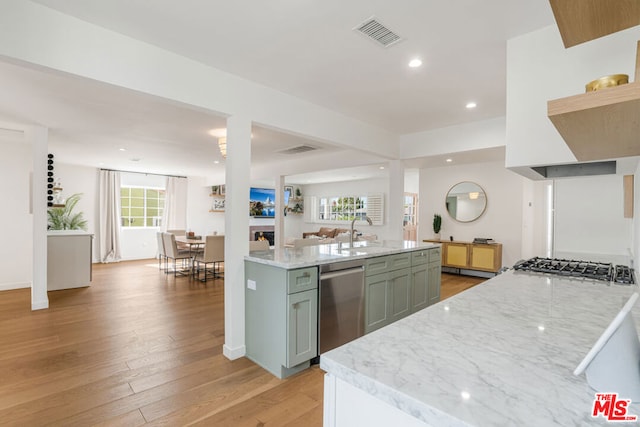 kitchen featuring stainless steel appliances, an island with sink, sink, and light stone counters