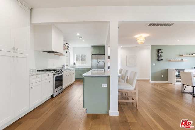 kitchen with stainless steel appliances, light hardwood / wood-style floors, an island with sink, white cabinets, and custom exhaust hood