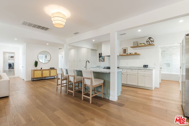 kitchen with light wood-type flooring, light stone counters, white cabinets, and a kitchen breakfast bar