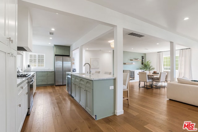 kitchen featuring an island with sink, a kitchen breakfast bar, green cabinets, stainless steel appliances, and light wood-type flooring