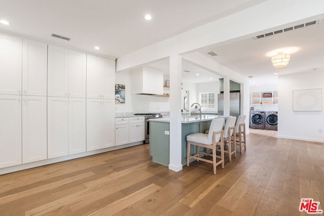 kitchen with white cabinetry, a kitchen breakfast bar, washing machine and clothes dryer, stainless steel appliances, and a center island with sink