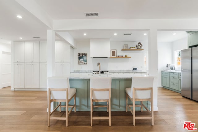 kitchen with green cabinets, a kitchen breakfast bar, stainless steel refrigerator, and light wood-type flooring