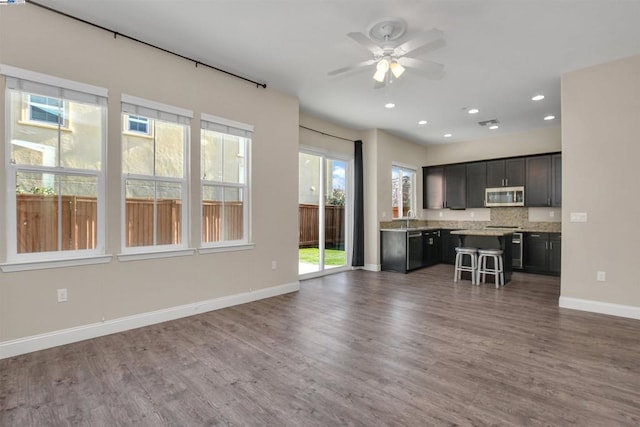 kitchen featuring a kitchen breakfast bar, hardwood / wood-style flooring, ceiling fan, stainless steel appliances, and backsplash