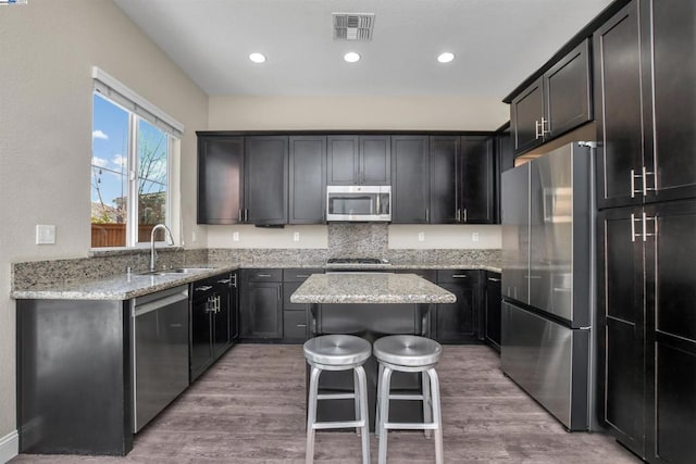 kitchen with appliances with stainless steel finishes, light stone countertops, sink, and a kitchen island