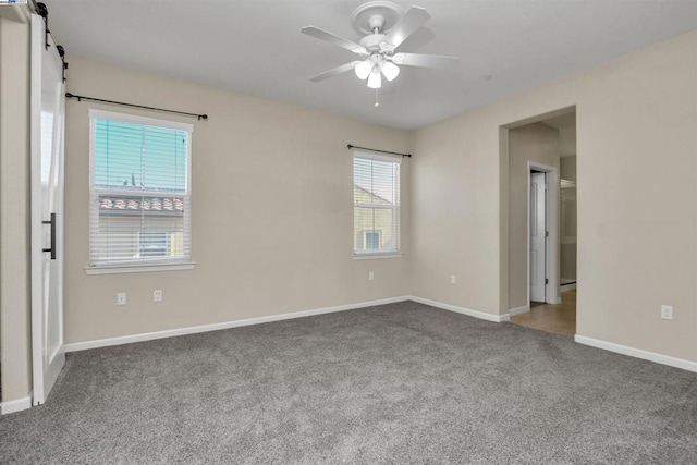 empty room featuring a barn door, carpet flooring, and ceiling fan