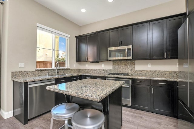 kitchen featuring a breakfast bar, sink, a center island, light stone counters, and stainless steel appliances