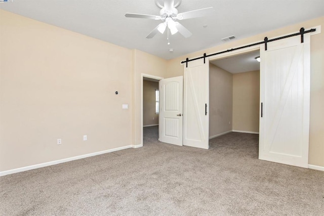 unfurnished bedroom featuring ceiling fan, a barn door, and light colored carpet