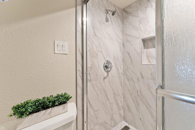 bathroom with a tile shower and toilet