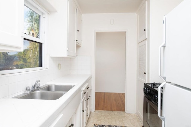 kitchen featuring sink, stainless steel gas range, white refrigerator, tasteful backsplash, and white cabinets