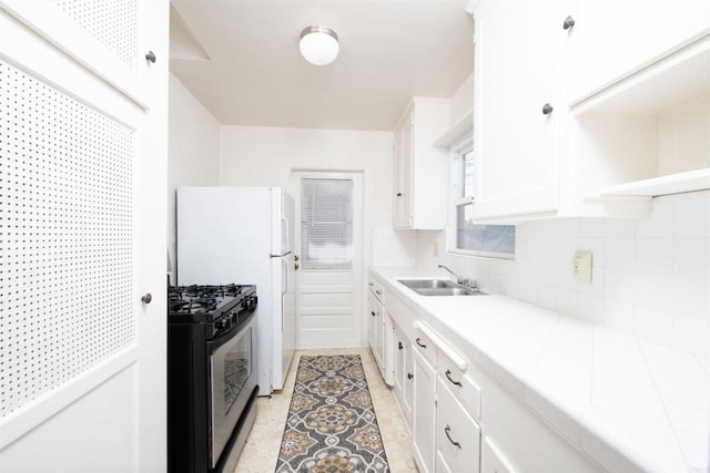 kitchen with gas range, tile counters, sink, and white cabinets