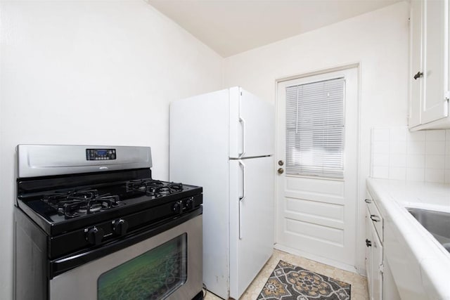 kitchen with light tile patterned flooring, stainless steel range with gas cooktop, white cabinets, decorative backsplash, and white fridge