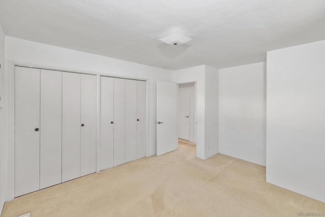 unfurnished bedroom with multiple closets and light carpet