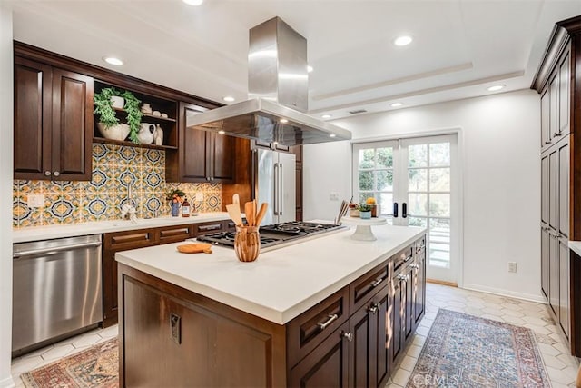 kitchen featuring appliances with stainless steel finishes, dark brown cabinets, tasteful backsplash, island range hood, and a kitchen island