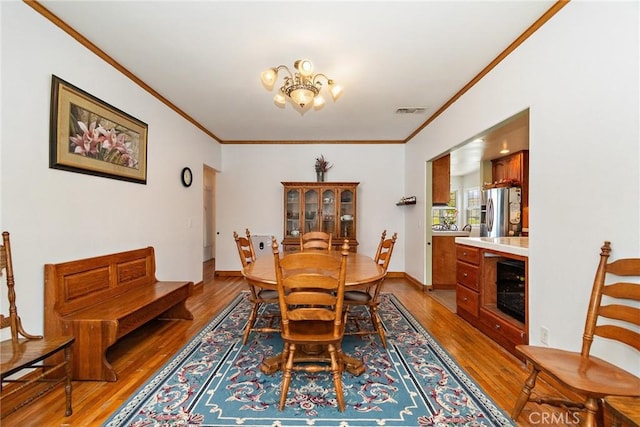 dining space featuring hardwood / wood-style flooring, ornamental molding, beverage cooler, and an inviting chandelier