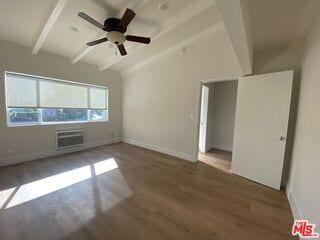 empty room featuring an AC wall unit, vaulted ceiling with beams, dark wood-type flooring, and ceiling fan