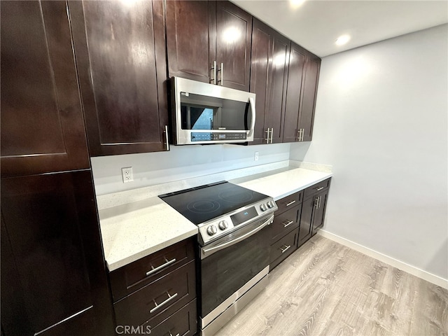 kitchen featuring dark brown cabinets, light wood-type flooring, light stone countertops, and appliances with stainless steel finishes