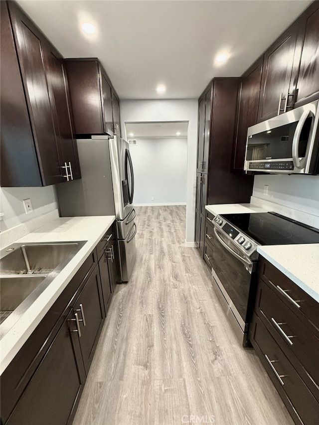 kitchen featuring appliances with stainless steel finishes, sink, light stone counters, dark brown cabinets, and light wood-type flooring