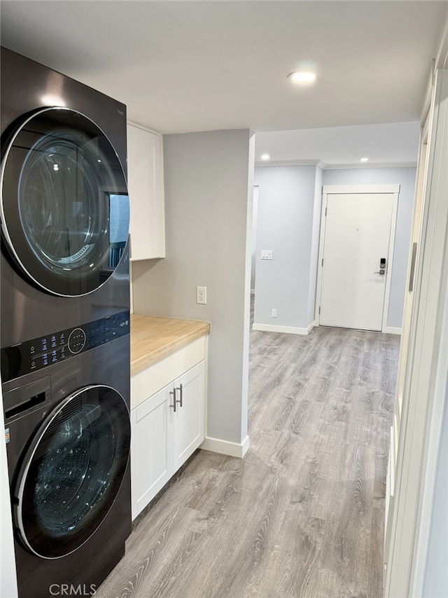 clothes washing area with stacked washer / dryer, cabinets, and light hardwood / wood-style flooring