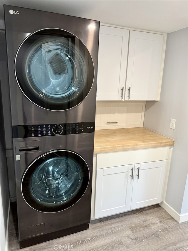 laundry area with stacked washer / drying machine, cabinets, and light wood-type flooring