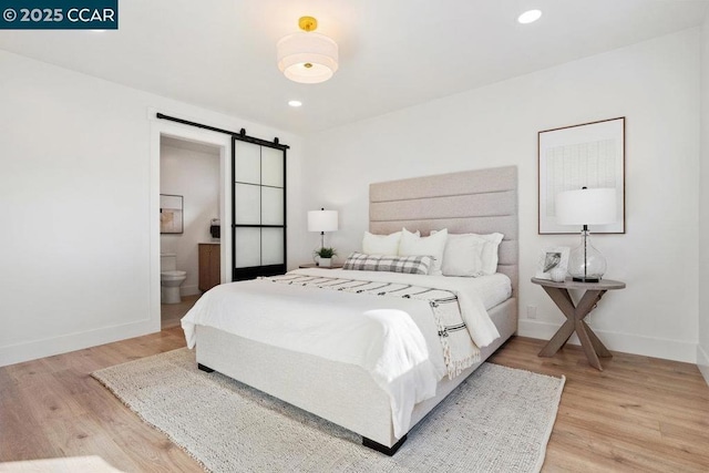 bedroom with light wood-type flooring, a barn door, and ensuite bathroom