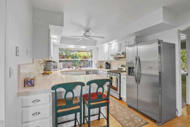 kitchen with a breakfast bar, light wood-type flooring, kitchen peninsula, stainless steel appliances, and white cabinets