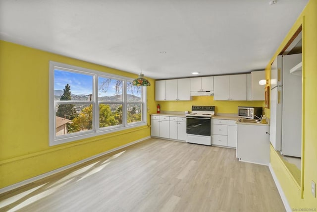 kitchen with pendant lighting, white appliances, white cabinets, and light wood-type flooring