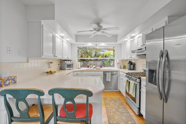 kitchen with stainless steel appliances, tasteful backsplash, white cabinets, a kitchen bar, and kitchen peninsula