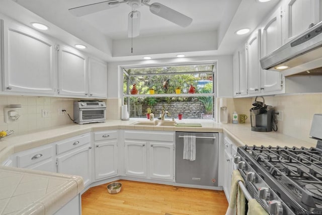 kitchen with white cabinetry, tile countertops, ventilation hood, light hardwood / wood-style flooring, and appliances with stainless steel finishes