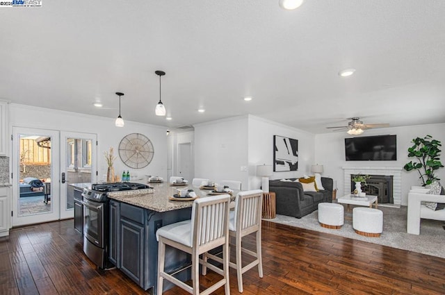 kitchen with a kitchen island, a breakfast bar area, light stone counters, dark wood-type flooring, and stainless steel range with gas stovetop