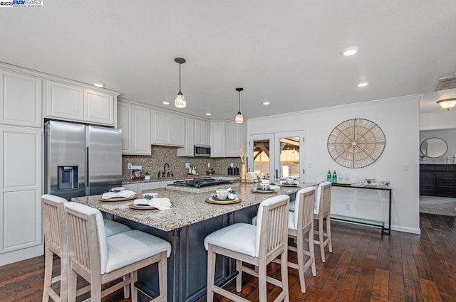 kitchen featuring white cabinetry, light stone counters, hanging light fixtures, dark hardwood / wood-style flooring, and stainless steel appliances