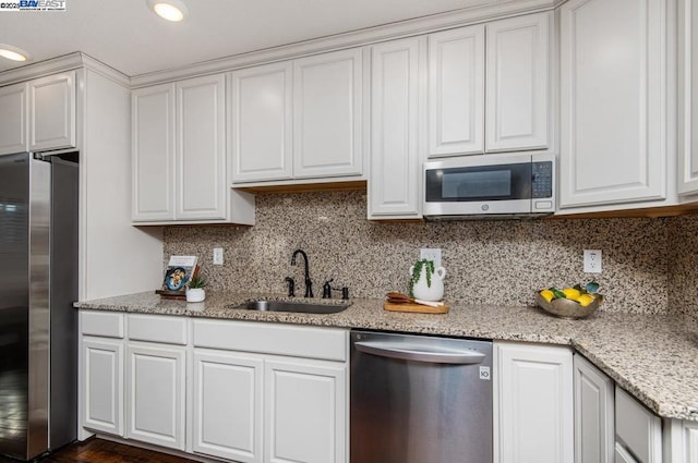 kitchen featuring appliances with stainless steel finishes, sink, white cabinets, decorative backsplash, and light stone countertops