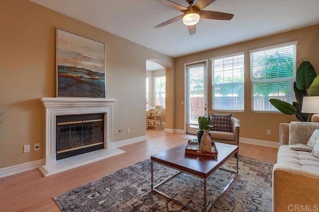 living room with a tile fireplace, ceiling fan, and light wood-type flooring